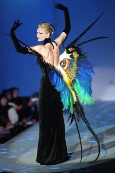 a woman is walking down the runway in a black dress with colorful feathers on it