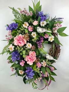 a wreath with pink, purple and white flowers is hanging on the wall next to a bird's nest