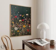 a table with a lamp and a painting on it next to a chair in front of a window