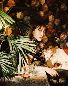 a woman sitting at a table in front of a plant