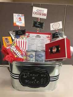 a bucket filled with candy and snacks on top of a table next to a sign