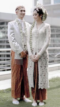 two people standing next to each other in front of a building with grass and buildings behind them