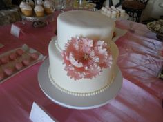 a white cake with pink flowers on it sitting on top of a table next to cupcakes