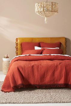 a bed with red bedspread and white pillows in a room that has beige walls