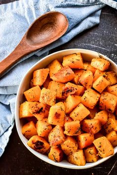 a white bowl filled with roasted potatoes on top of a table next to a wooden spoon