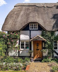 a thatched roof house with white trim and flowers on the front door, surrounded by greenery