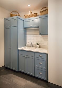 an empty kitchen with blue cabinets and white counter tops is pictured in this image, there are baskets on top of the cupboards