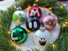 christmas ornaments with mario and luigi faces on them in a snow - covered circle surrounded by evergreen branches