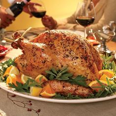 a roasted turkey on a platter with oranges and herbs