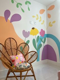 a wicker chair sitting in front of a wall with flowers painted on the walls