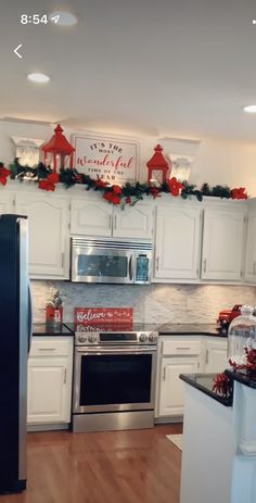 a kitchen decorated for christmas with white cabinets and silver appliances