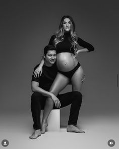 a pregnant woman sitting on top of a stool next to a man in black shirt