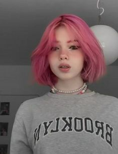 a young woman with pink hair wearing a grey brooklyn sweatshirt and pearl necklace, posing for the camera