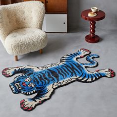 a rug with a blue tiger on the floor next to a chair and side table