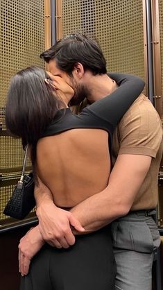 a man and woman embracing each other in front of a wall with gold mesh covering it