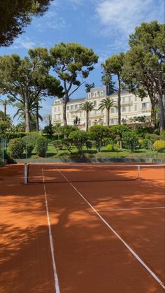 a tennis court surrounded by trees with a building in the background