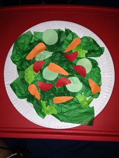 a paper plate topped with lettuce and carrots on top of a red table