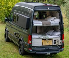 the back end of a van with several beds in it's cargo compartment, parked on grass