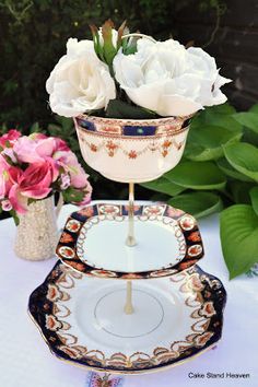 white roses are in an ornate glass vase on a table next to other plates and flowers