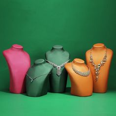 three different colored vases with necklaces on them in front of a green background