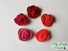 four crocheted roses sitting on top of a white table next to each other