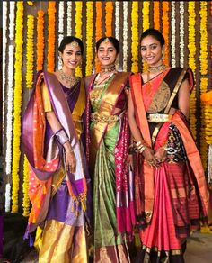 three women standing next to each other in front of flowers