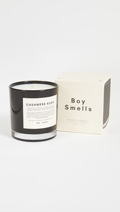 a black candle sitting next to a box on a white surface with the words boy smells printed on it