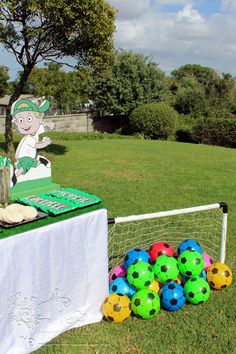 a table topped with soccer balls next to a net filled with cake and cupcakes