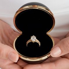 a close up of a person holding an engagement ring in a black and gold box