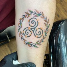 a tattoo on the leg of a woman with an orange and green wreath around it