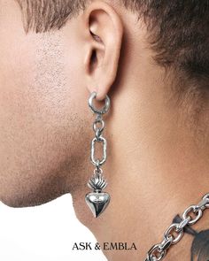 a close up of a man wearing a chain and heart shaped earring