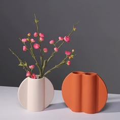 two vases with pink flowers in them on a white table next to each other