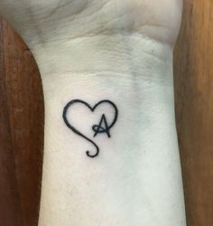 a small heart tattoo on the wrist with an arrow in the shape of a heart