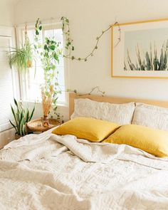 a bed with white sheets and yellow pillows in a bedroom next to a potted plant