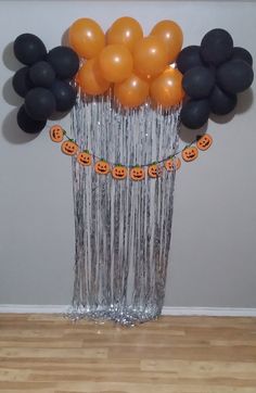 an arrangement of halloween balloons and streamers in a vase on a wooden floor with a wall behind it