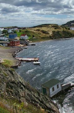 boats are docked on the water in front of small houses and cliffs with cloudy skies