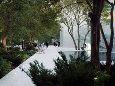 people are sitting on benches in the middle of a park with trees and bushes around them