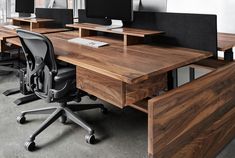 an office desk with two computer monitors on it and a chair in the foreground