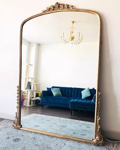 a large gold framed mirror sitting on top of a floor next to a blue couch