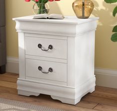 a white nightstand with two drawers on top of it next to a potted plant