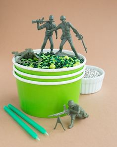 two toy soldiers are in a green container with rocks and plastic pencils next to it