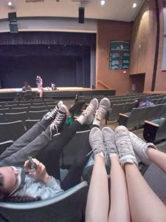 two people laying on their stomachs in front of an empty auditorium with one person holding a cell phone