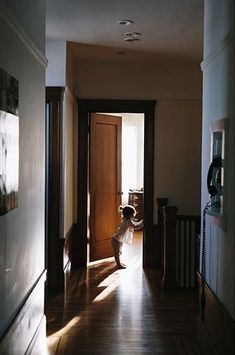 a young child is sitting on the floor in an empty hallway with sunlight coming through the door