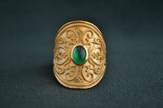 This shield-type byzantine ring is entirely made with solid Sterling Silver (925 Silver). It has a 22K-gold plating, and there are patterns engraved all over the ring. The stone in the center of the ring is an oval Cubic Zirconia Emerald (or any stone of your request). The dimensions of the ring are 2.5cm height x 2cm width. It can be worn on the middle finger also. Byzantine Gold Emerald Ring For Anniversary, Byzantine Gold Emerald Anniversary Ring, Byzantine Ring With Intricate Design For Gift, Byzantine Rings With Intricate Design For Gift, Byzantine Style Ring With Intricate Design As Gift, Byzantine Intaglio Ring For Anniversary, Wedding Rings With Byzantine Intricate Design, Byzantine Wedding Rings With Intricate Design, Hallmarked 22k Gold Byzantine Rings