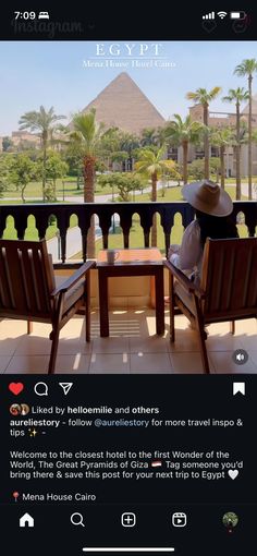 two wooden chairs sitting on top of a balcony next to a table with a hat on it