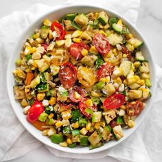 a white bowl filled with corn, tomatoes and zucchini salad on top of a white napkin