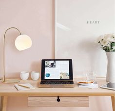 a laptop computer sitting on top of a wooden desk next to a vase with flowers