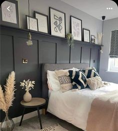 a bedroom with gray walls and pictures on the wall above the bed, along with a small side table