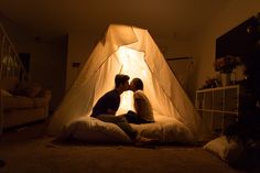 two people sitting on pillows in front of a white tent with the lights turned on