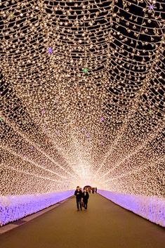 two people walking down a walkway covered in lights and streaming from the ceiling to the ground